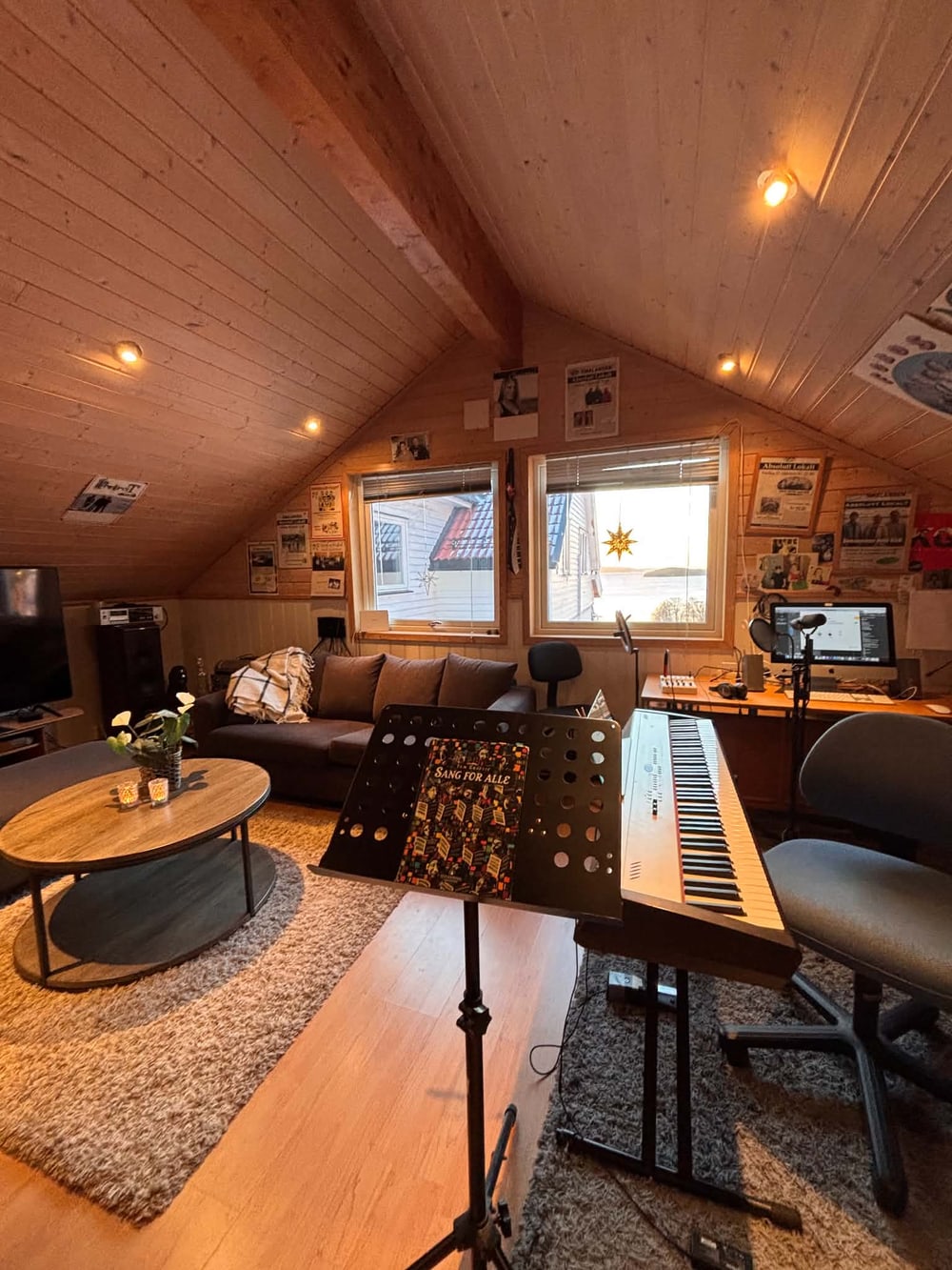 Studioet på Tofte med keyboard, notestativ og sofa under skråtaket.